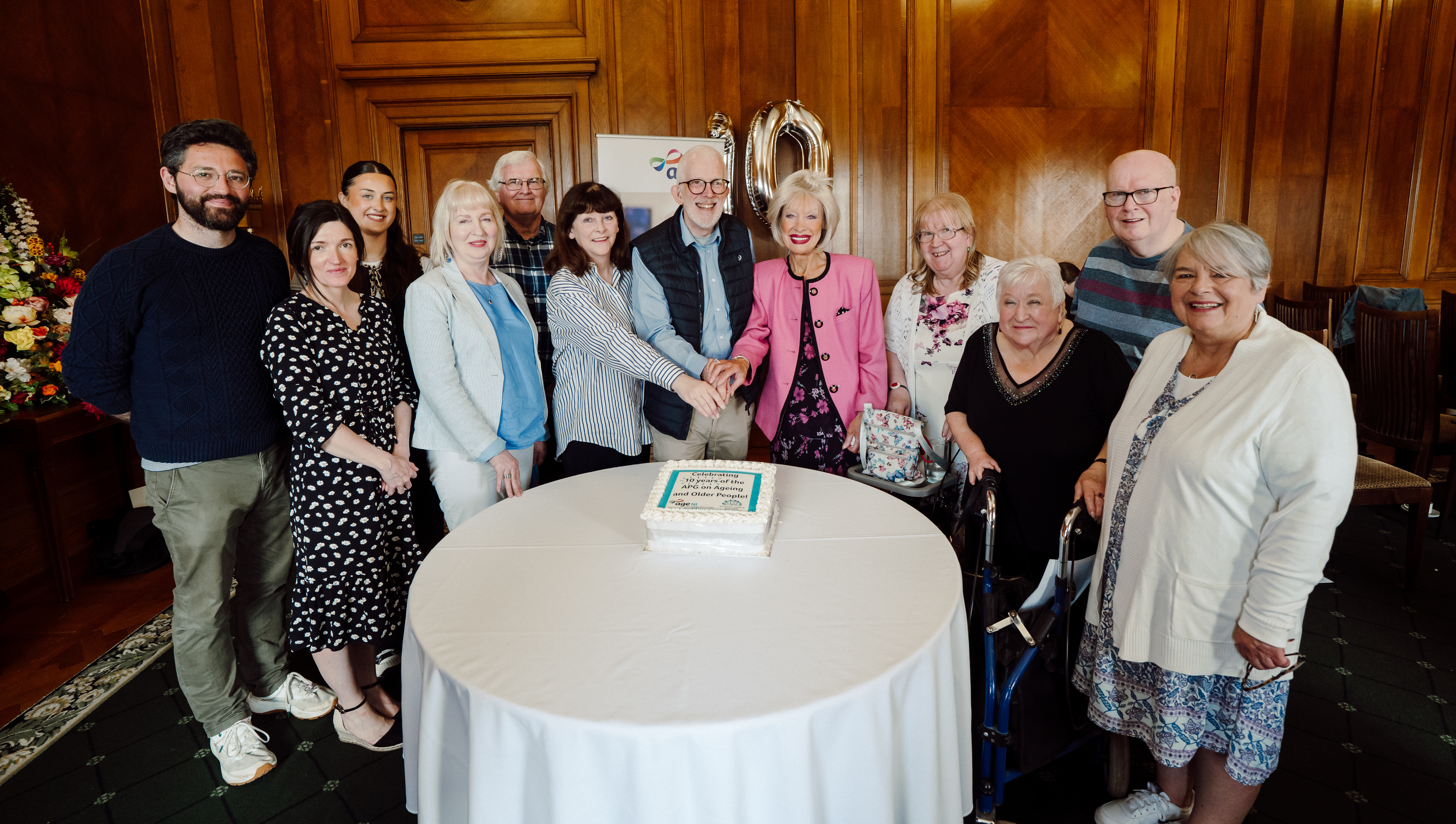 group of people around a cake that says "Celebrating 10 years of the APG on Ageing and Older People!"