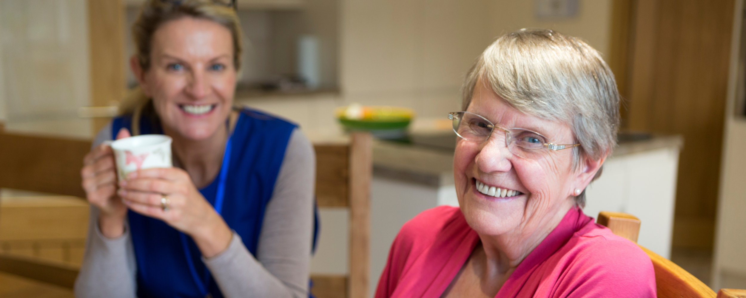older woman and a care worker sitting at a table smiling