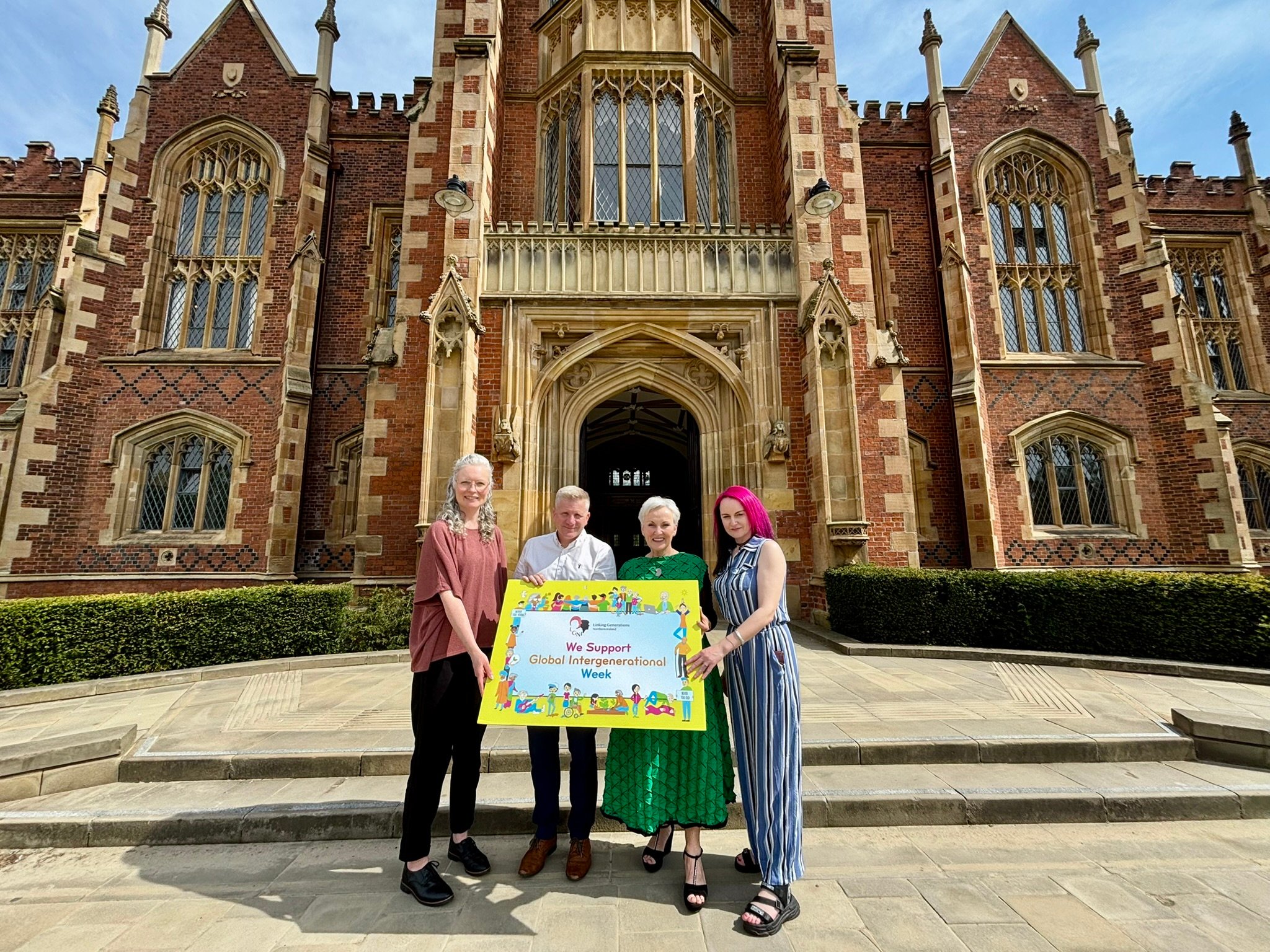 four people standing outside a university building holding a "Global Intergenerational Week" logo board