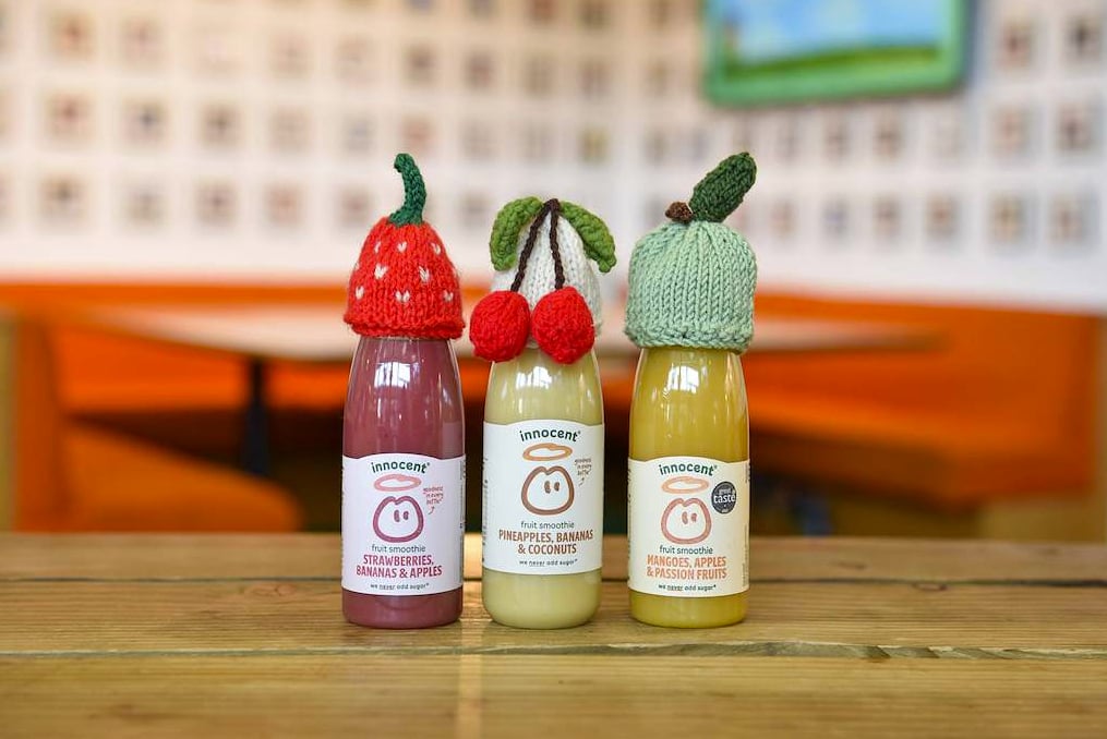 smoothie bottles sitting on a table with small knitted hats over the caps
