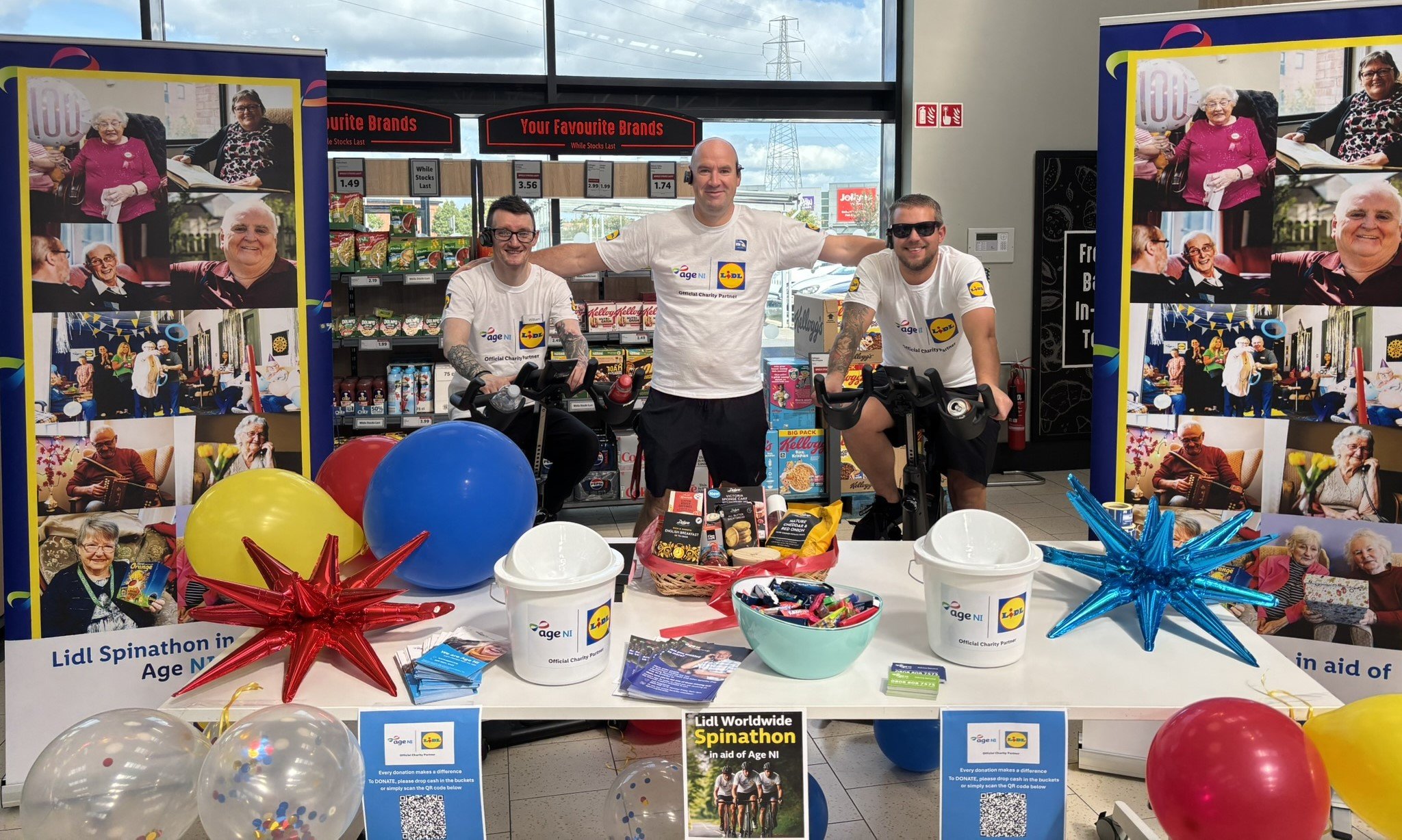 Lidl employees in branded tshirts on stationary bikes in Lidl store with banners balloons and posters promoting charity partnership