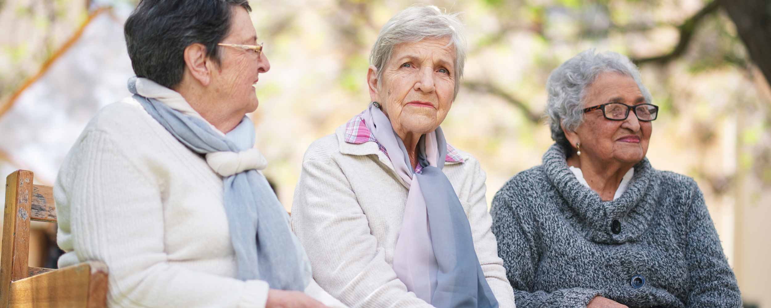 three older women sitting on a bench outside