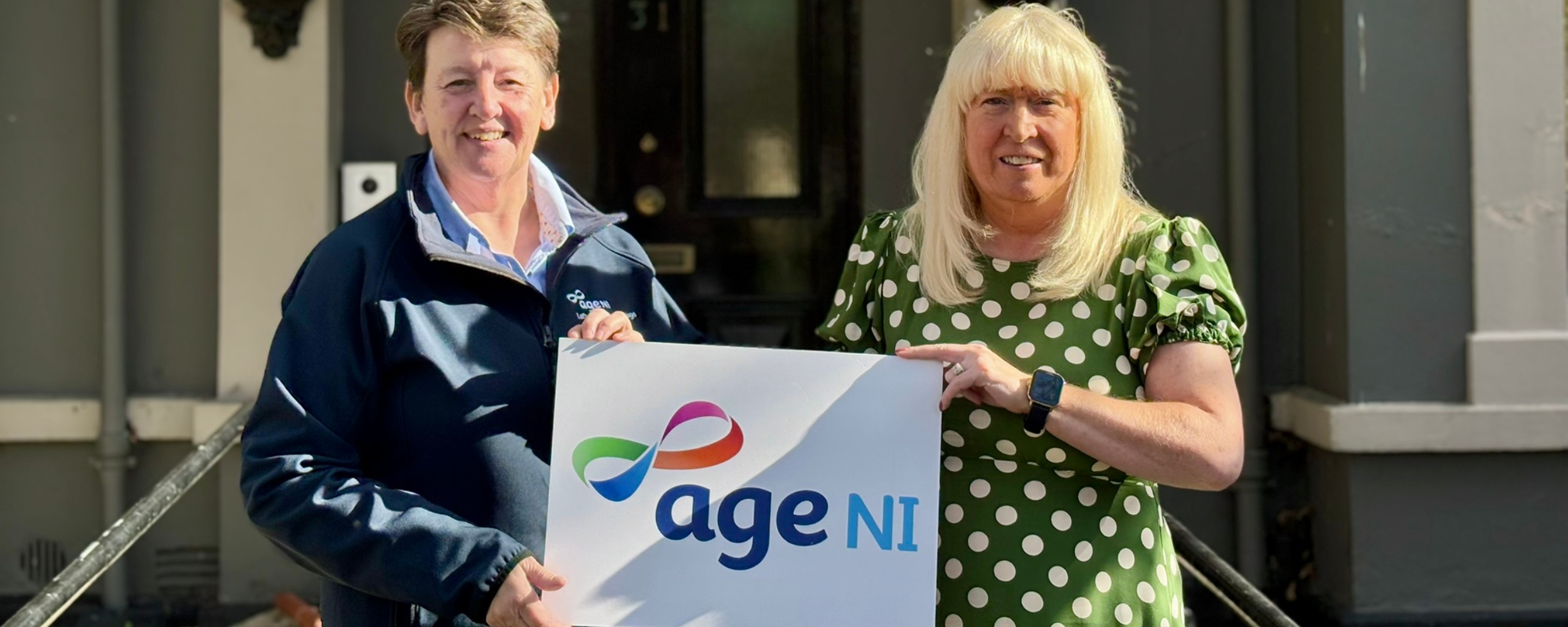 two woman outside holding Age NI logo board