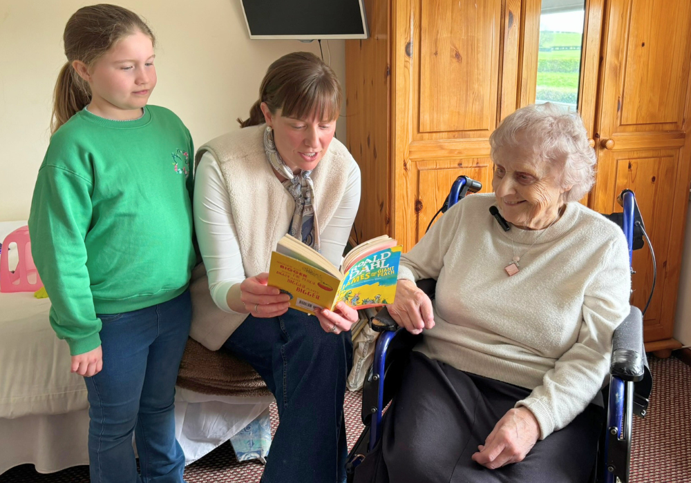 woman reading to an older woman and a young girl