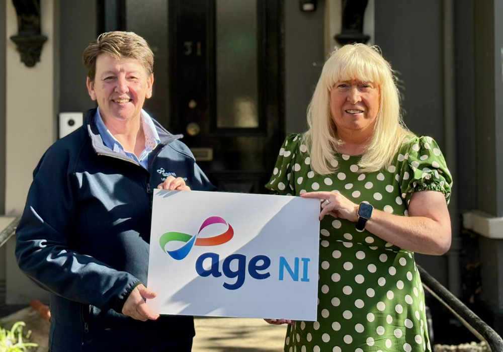 two woman standing outside holding Age NI logo board
