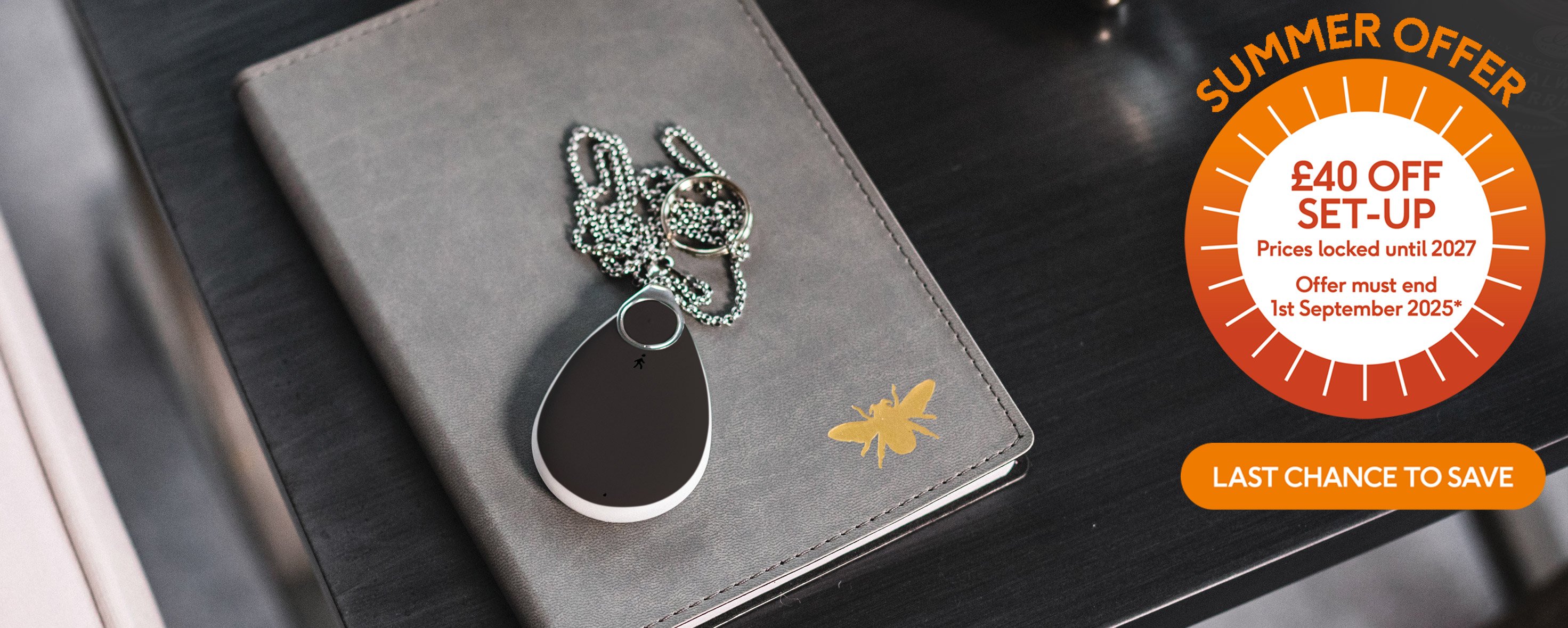 Fall alarm pendant sitting on a notebook on a desk, orange banner in corner "£40 off setup extended for a limited time only"