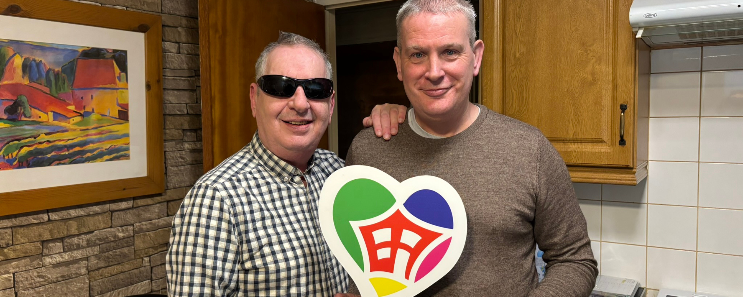 two older men holding a Shared Lives logo board