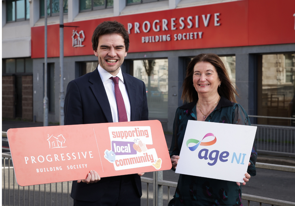 Progressive and Age NI staff standing outside Progressive building holding logo boards